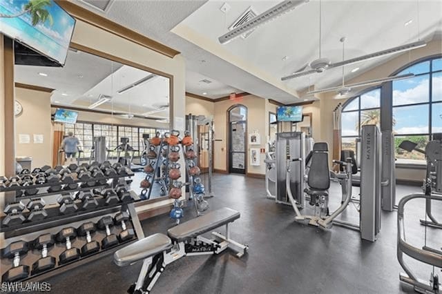 workout area featuring visible vents, ornamental molding, a ceiling fan, baseboards, and vaulted ceiling