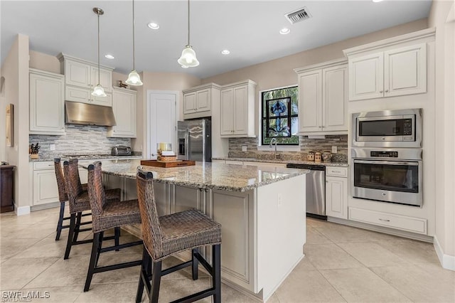 kitchen with a center island, under cabinet range hood, a breakfast bar area, light stone counters, and appliances with stainless steel finishes