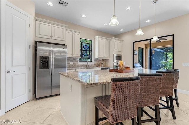 kitchen featuring visible vents, a kitchen island, light tile patterned flooring, stainless steel appliances, and tasteful backsplash