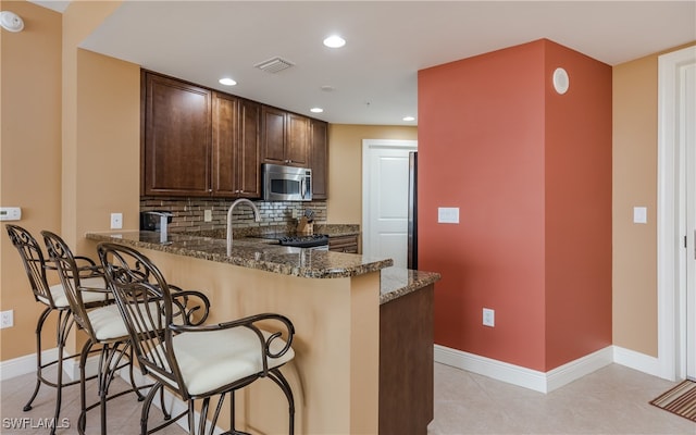 kitchen featuring kitchen peninsula, a kitchen bar, fridge, backsplash, and dark stone countertops