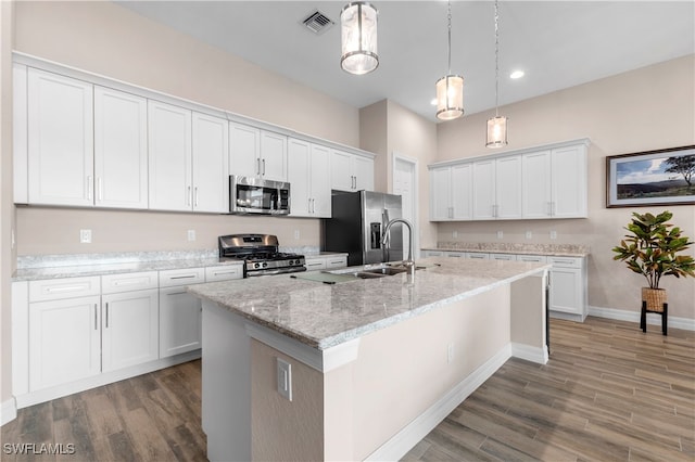 kitchen with an island with sink, stainless steel appliances, white cabinetry, and dark hardwood / wood-style flooring