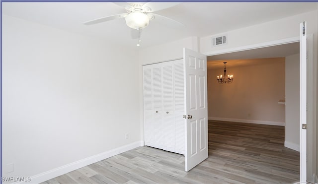 unfurnished bedroom featuring ceiling fan with notable chandelier, a closet, and light hardwood / wood-style flooring