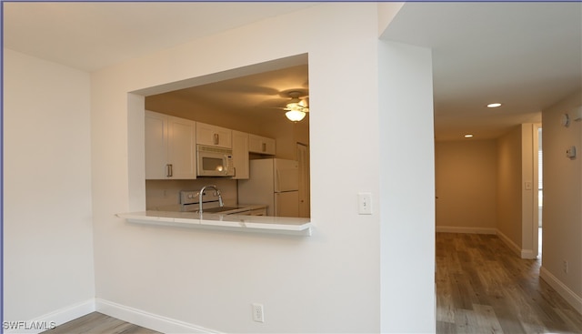 kitchen featuring ceiling fan, white cabinets, kitchen peninsula, white appliances, and hardwood / wood-style floors