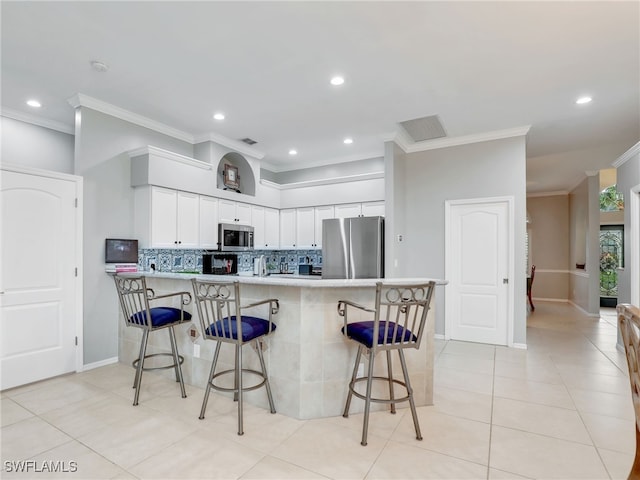 kitchen featuring ornamental molding, stainless steel appliances, white cabinets, kitchen peninsula, and a breakfast bar area