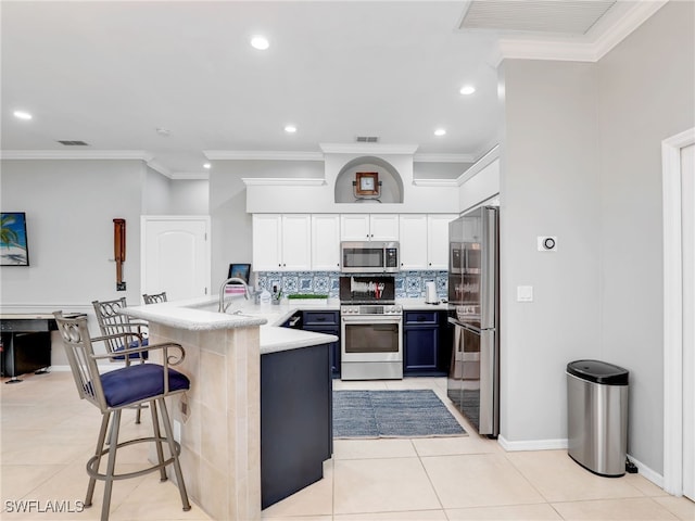 kitchen featuring white cabinets, ornamental molding, a kitchen breakfast bar, light tile patterned flooring, and appliances with stainless steel finishes