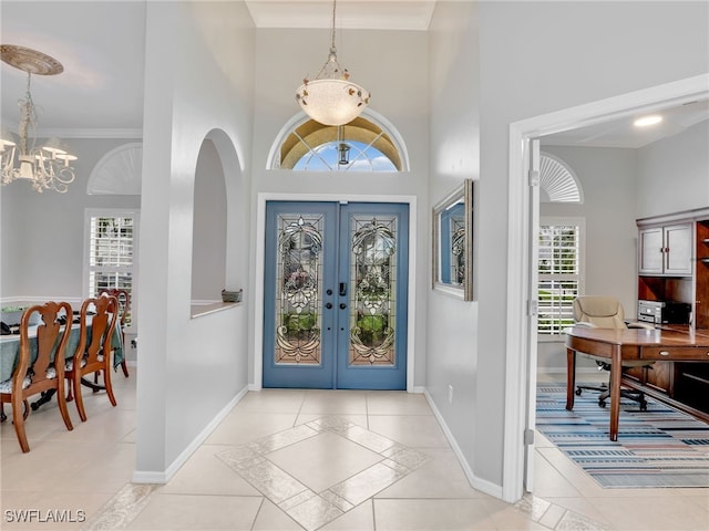 entryway with a towering ceiling, a chandelier, french doors, and crown molding