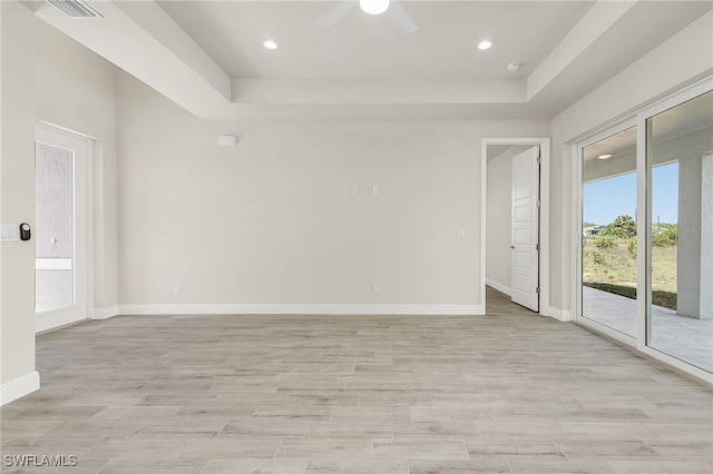 empty room with a raised ceiling, ceiling fan, and light hardwood / wood-style flooring