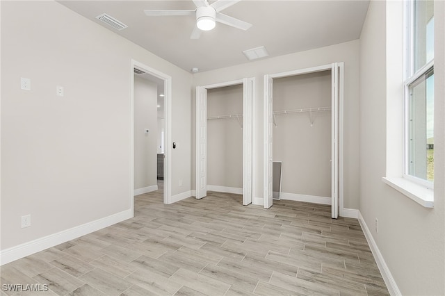 unfurnished bedroom featuring ceiling fan, multiple closets, and light wood-type flooring