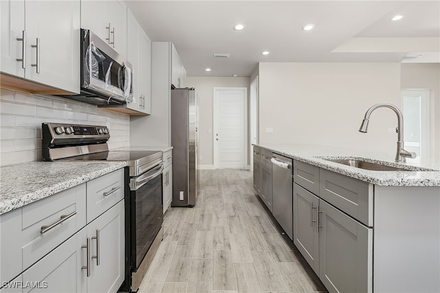 kitchen featuring light stone counters, a sink, tasteful backsplash, appliances with stainless steel finishes, and light wood-type flooring