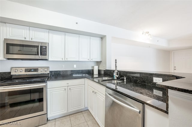 kitchen with appliances with stainless steel finishes, sink, light tile patterned floors, dark stone countertops, and white cabinets