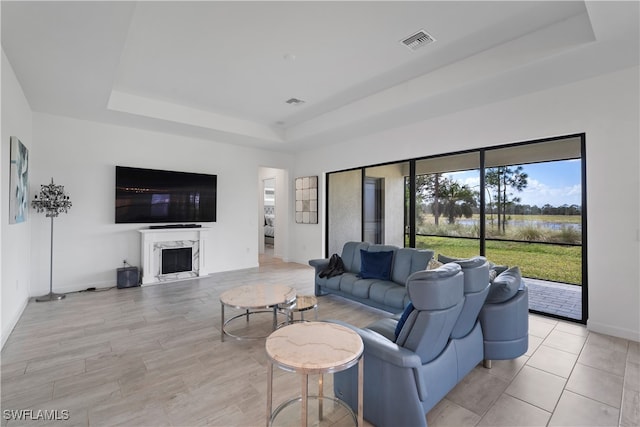 living room with light hardwood / wood-style floors, a high end fireplace, and a tray ceiling