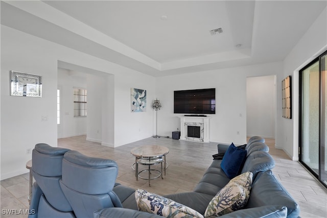 living room featuring a raised ceiling, a premium fireplace, and light wood-type flooring