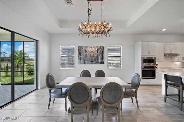 dining space with a notable chandelier, light tile patterned floors, and a raised ceiling