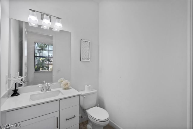 half bathroom featuring toilet, baseboards, and vanity