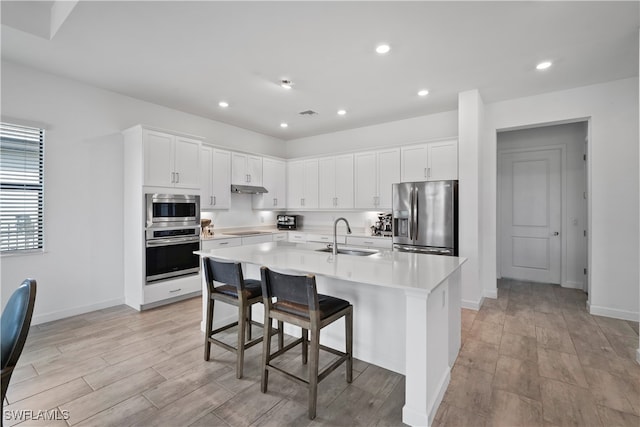 kitchen with a breakfast bar, white cabinetry, a kitchen island with sink, sink, and stainless steel appliances