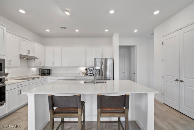 kitchen with light hardwood / wood-style floors, white cabinets, stainless steel appliances, and a center island with sink