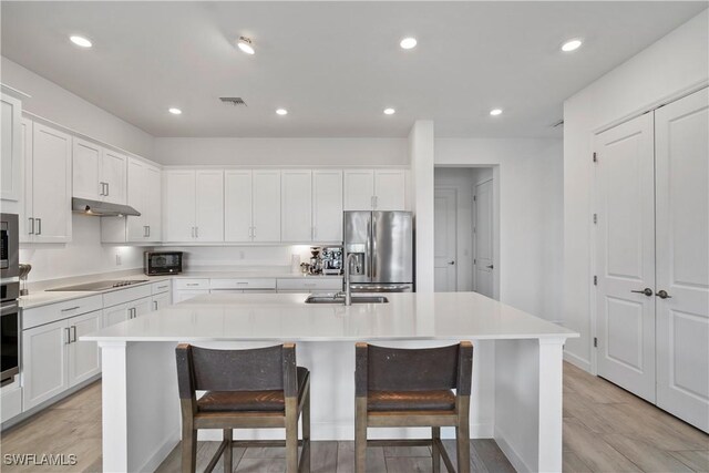 kitchen featuring an island with sink, appliances with stainless steel finishes, light countertops, under cabinet range hood, and a sink