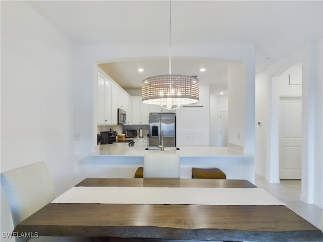 kitchen featuring white cabinetry, kitchen peninsula, appliances with stainless steel finishes, a notable chandelier, and decorative light fixtures