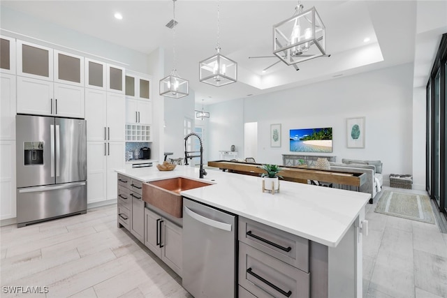 kitchen with gray cabinetry, white cabinets, stainless steel appliances, decorative light fixtures, and a kitchen island with sink