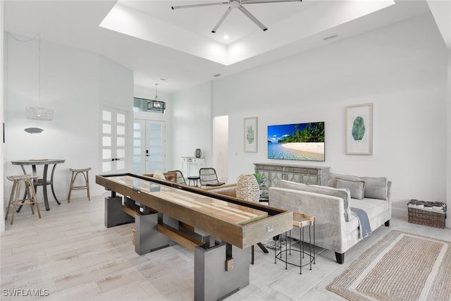 recreation room featuring ceiling fan, light hardwood / wood-style flooring, and a towering ceiling