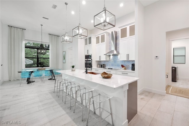 kitchen with a kitchen island with sink, white cabinetry, hanging light fixtures, wall chimney exhaust hood, and black electric cooktop