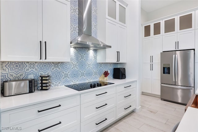 kitchen with white cabinetry, backsplash, wall chimney range hood, black electric stovetop, and stainless steel fridge with ice dispenser