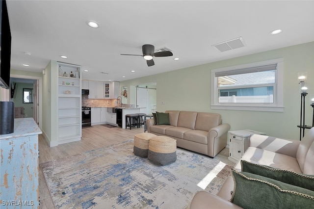 living room with a barn door, light hardwood / wood-style flooring, ceiling fan, and sink