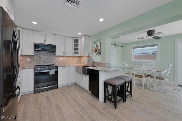 kitchen featuring black appliances, kitchen peninsula, a barn door, range hood, and white cabinetry