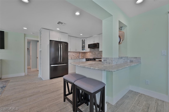 kitchen featuring stainless steel appliances, kitchen peninsula, light hardwood / wood-style floors, a kitchen bar, and white cabinets