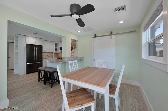 dining area with a barn door, light hardwood / wood-style floors, and ceiling fan