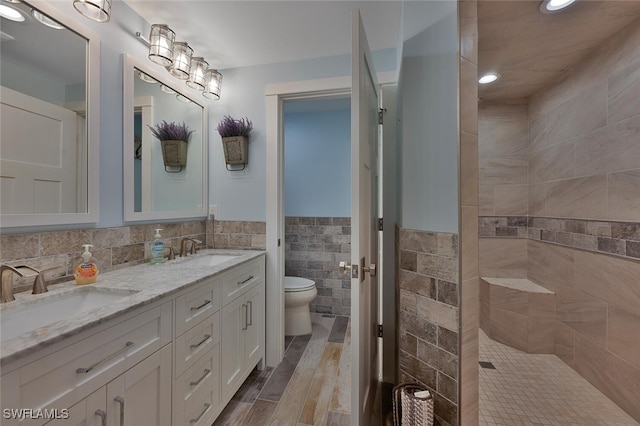 bathroom with hardwood / wood-style floors, vanity, toilet, tiled shower, and tile walls