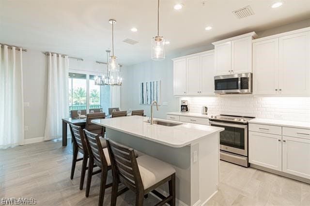 kitchen featuring white cabinets, an island with sink, decorative light fixtures, a chandelier, and stainless steel appliances