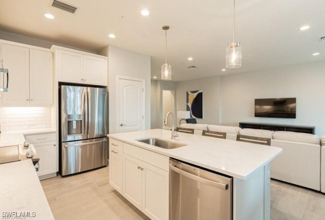 kitchen featuring an island with sink, sink, white cabinets, hanging light fixtures, and stainless steel appliances