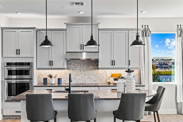 kitchen featuring gray cabinetry, stainless steel double oven, hanging light fixtures, and stone counters