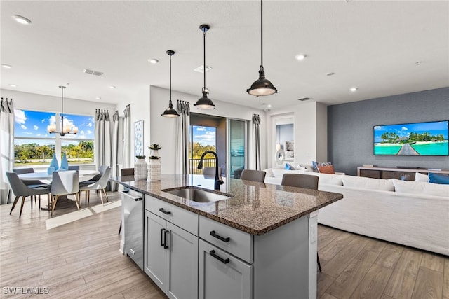 kitchen with dark stone countertops, a center island with sink, hanging light fixtures, and sink