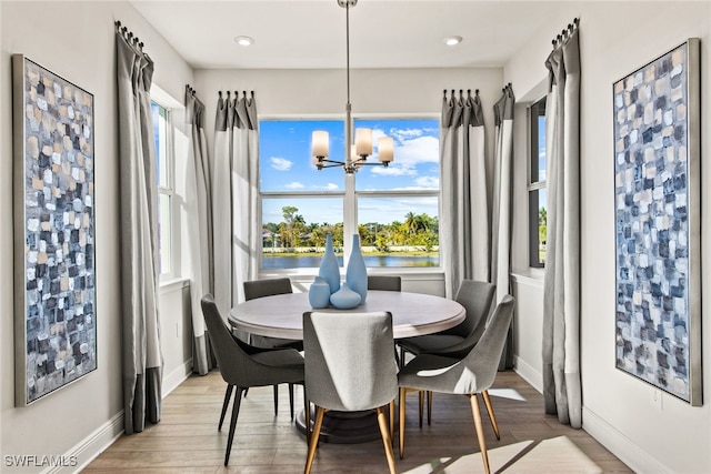 dining area featuring an inviting chandelier, a water view, and light hardwood / wood-style floors