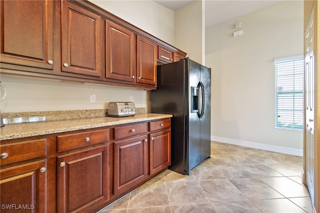 kitchen with light stone countertops, light tile patterned flooring, and black fridge