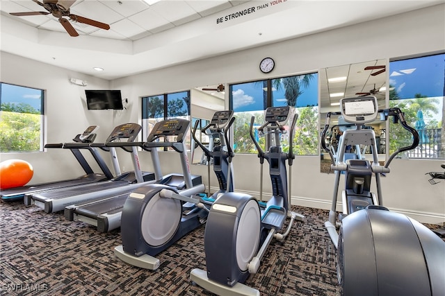 gym with a tray ceiling and dark colored carpet