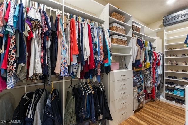 spacious closet featuring a wall mounted air conditioner and light hardwood / wood-style floors