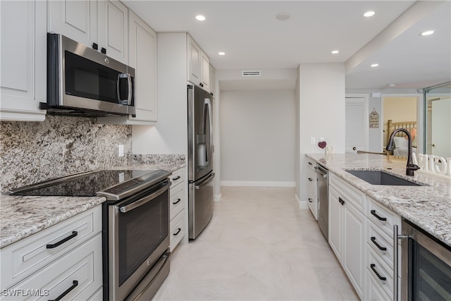 kitchen featuring white cabinets, sink, beverage cooler, stainless steel appliances, and light stone countertops