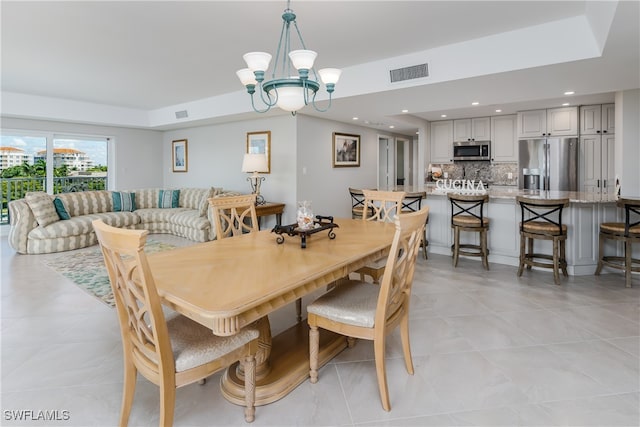 tiled dining room with an inviting chandelier and a raised ceiling