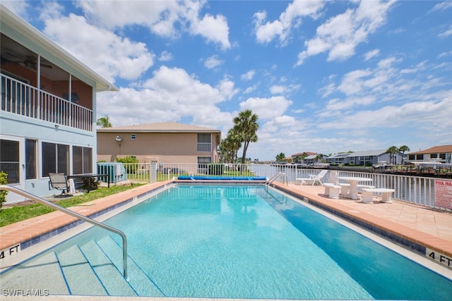 pool featuring a patio, a water view, and fence
