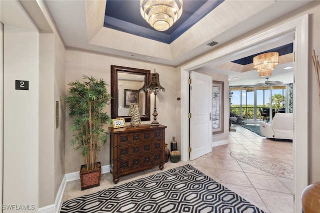 tiled entrance foyer featuring a raised ceiling and a chandelier