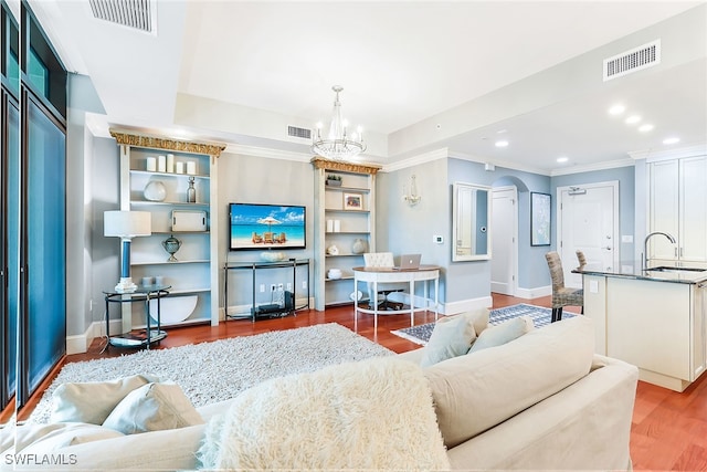 living room featuring sink, dark hardwood / wood-style floors, ornamental molding, a raised ceiling, and a chandelier