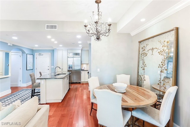 dining room featuring sink, wood-type flooring, ornamental molding, and a chandelier