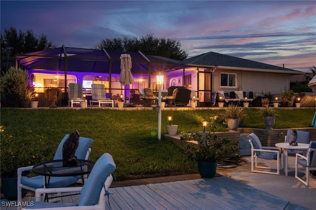 back house at dusk featuring a patio area, a wooden deck, and a lawn