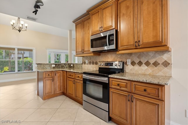 kitchen with a chandelier, stainless steel appliances, light stone counters, and backsplash