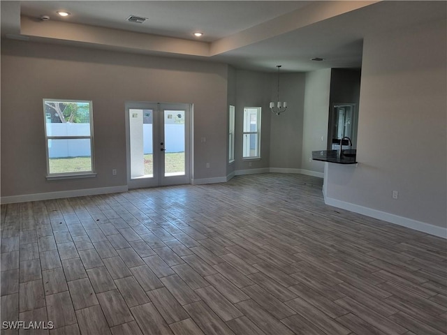 unfurnished living room featuring a towering ceiling, hardwood / wood-style floors, an inviting chandelier, and french doors