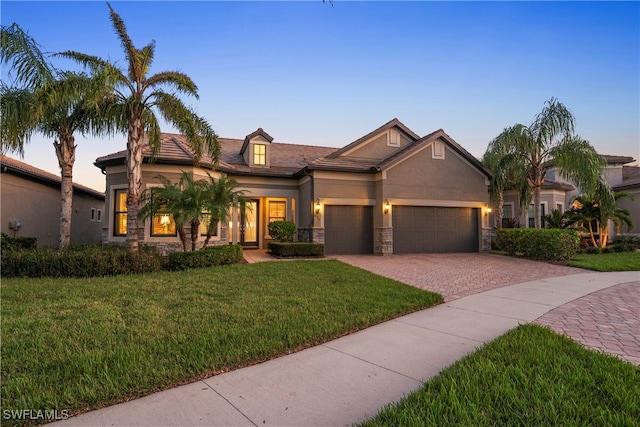 view of front facade featuring decorative driveway, a front yard, stone siding, and stucco siding