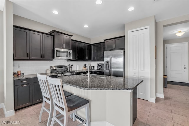 kitchen with tasteful backsplash, sink, an island with sink, appliances with stainless steel finishes, and dark stone countertops